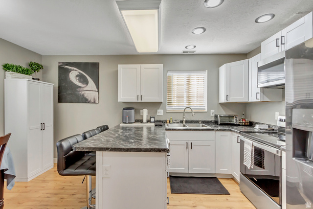 933 South Freedom Boulevard, Unit 7 Provo, UT 84601 - Photo 8 of 23 Kitchen featuring a kitchen bar, stainless steel appliances, white cabinets, updated paint and lights, and light wood-style floors