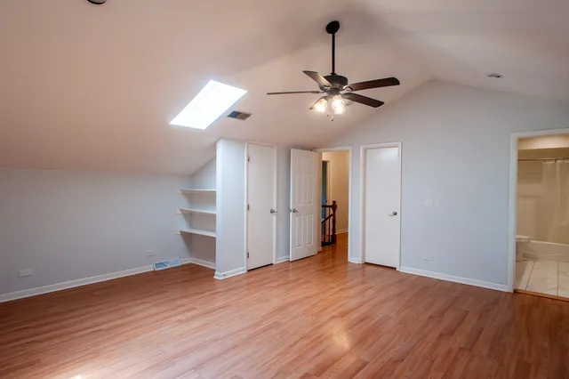 a view of an empty room with wooden floor and a ceiling fan