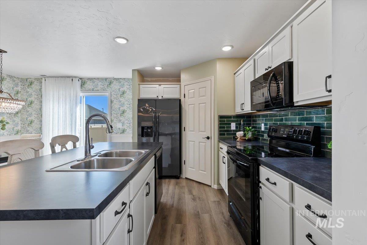12781 Ashfield Street Caldwell, ID 83607 - Photo 14 of 36 Kitchen with black appliances, dark countertops, a kitchen island with sink, white cabinetry, and dark wood-style floors