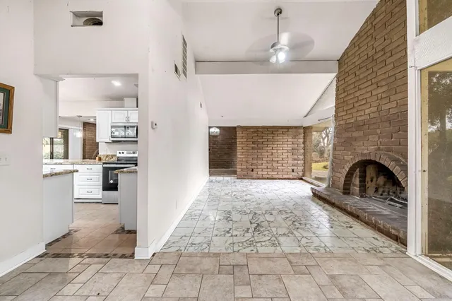 a view of a livingroom with a fireplace a ceiling fan and a kitchen view