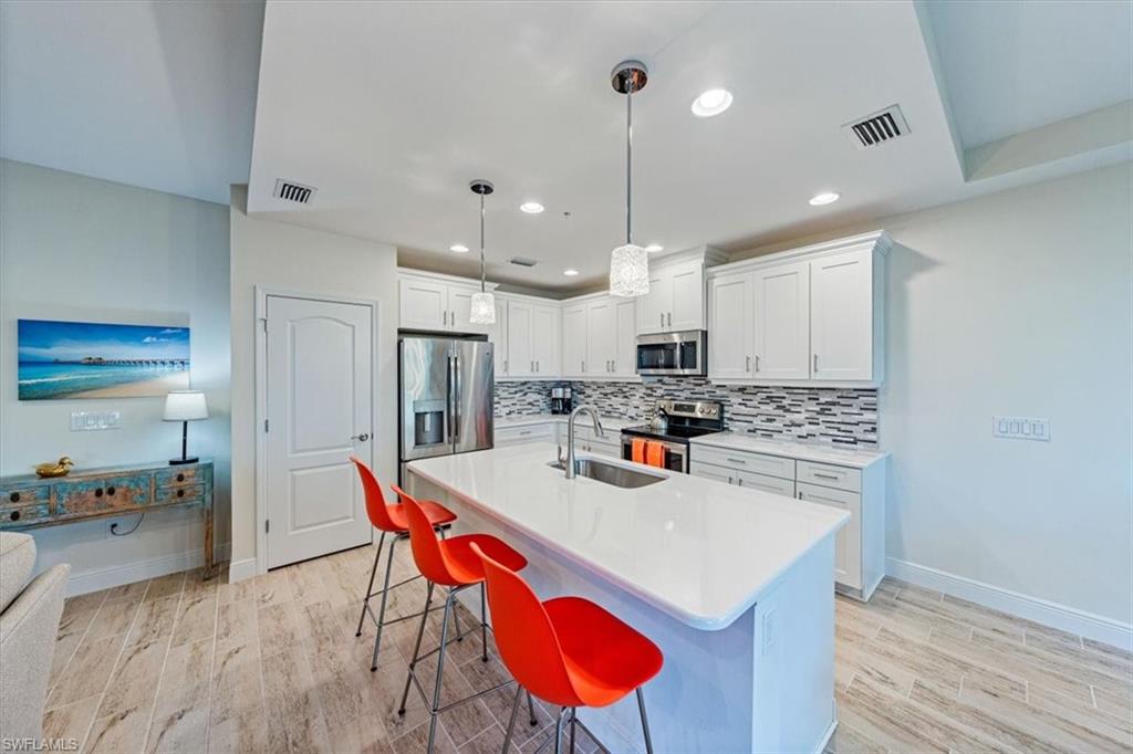 6934 Avalon Circle, Unit 402 Naples, FL 34112 - Photo 7 of 28 a kitchen with stainless steel appliances granite countertop a sink a stove a refrigerator and island with wooden floor