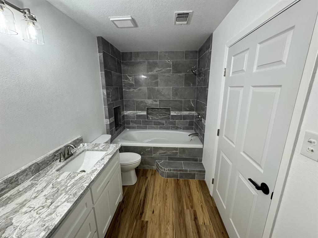 520 County Road Powderly, TX 75473 - Photo 23 of 24 Full bathroom featuring hardwood / wood-style floors, vanity, a textured ceiling, and tiled shower / bath
