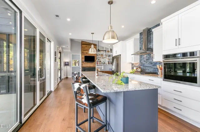 a kitchen with stainless steel appliances kitchen island granite countertop a stove a refrigerator a oven a sink a dining table and chairs with wooden floor