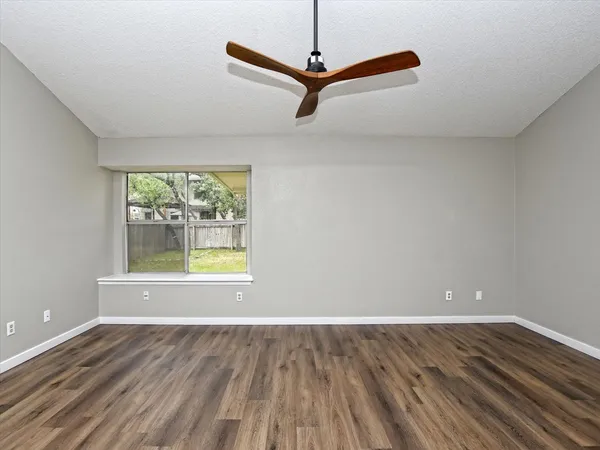 an empty room with wooden floor fan and windows