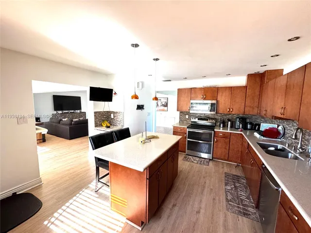 a kitchen with stainless steel appliances kitchen island granite countertop a stove top oven a sink a dining table and chairs with wooden floor