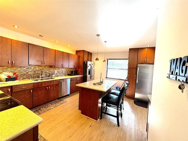 a kitchen with stainless steel appliances kitchen island granite countertop a table chairs and a refrigerator