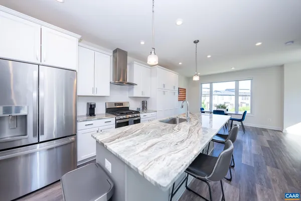 a kitchen with stainless steel appliances granite countertop a refrigerator a stove a sink a dining table and chairs with wooden floor