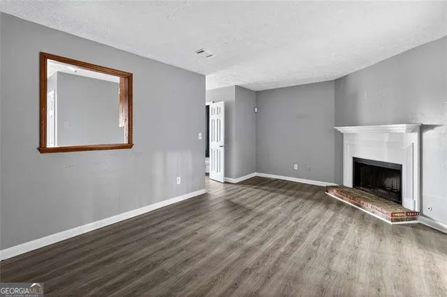 a view of an empty room with wooden floor fireplace and a window