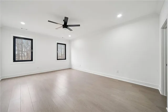 an empty room with wooden floor ceiling fan and windows