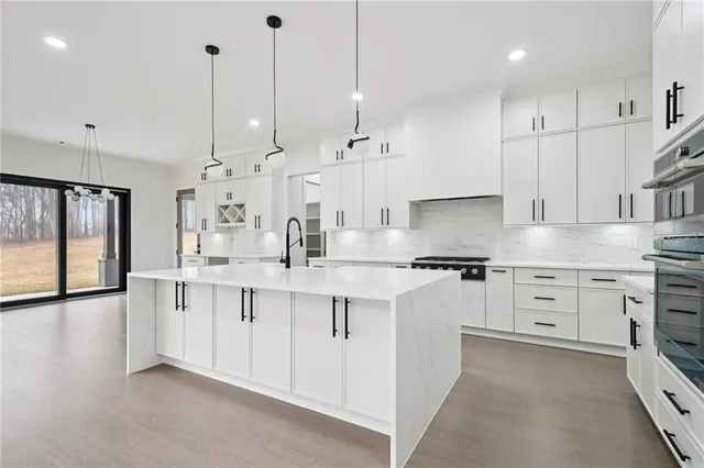 a kitchen with stainless steel appliances granite countertop a stove a sink and white cabinets with wooden floor