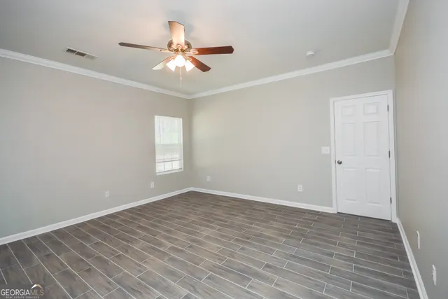 a view of an empty room with wooden floor and a ceiling fan