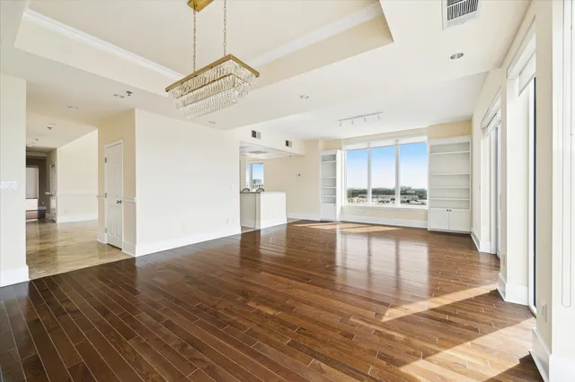 a view of an empty room and kitchen view with wooden floor