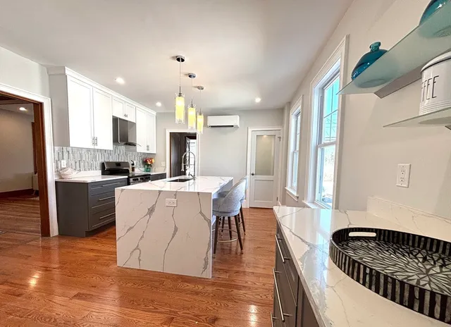 a living room with stainless steel appliances kitchen island granite countertop a refrigerator a stove a sink dishwasher and white cabinets with wooden floor