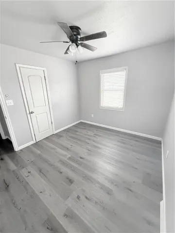 an empty room with wooden floor fan and windows