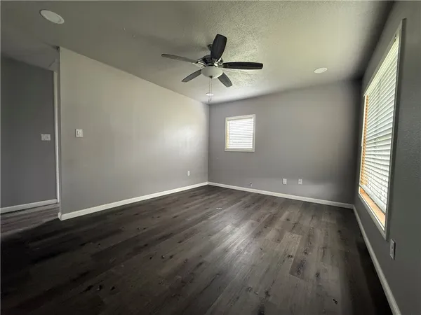 an empty room with wooden floor a ceiling fan and windows