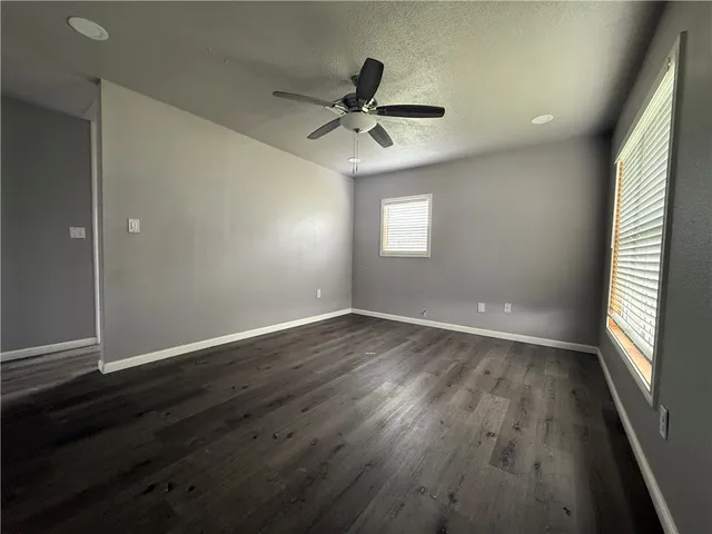 an empty room with wooden floor a ceiling fan and windows