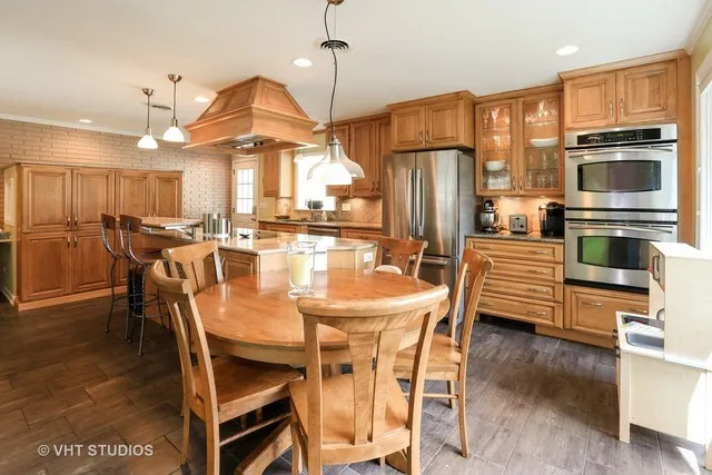 a kitchen with stainless steel appliances granite countertop a stove a refrigerator a oven a sink a dining table and chairs with wooden floor