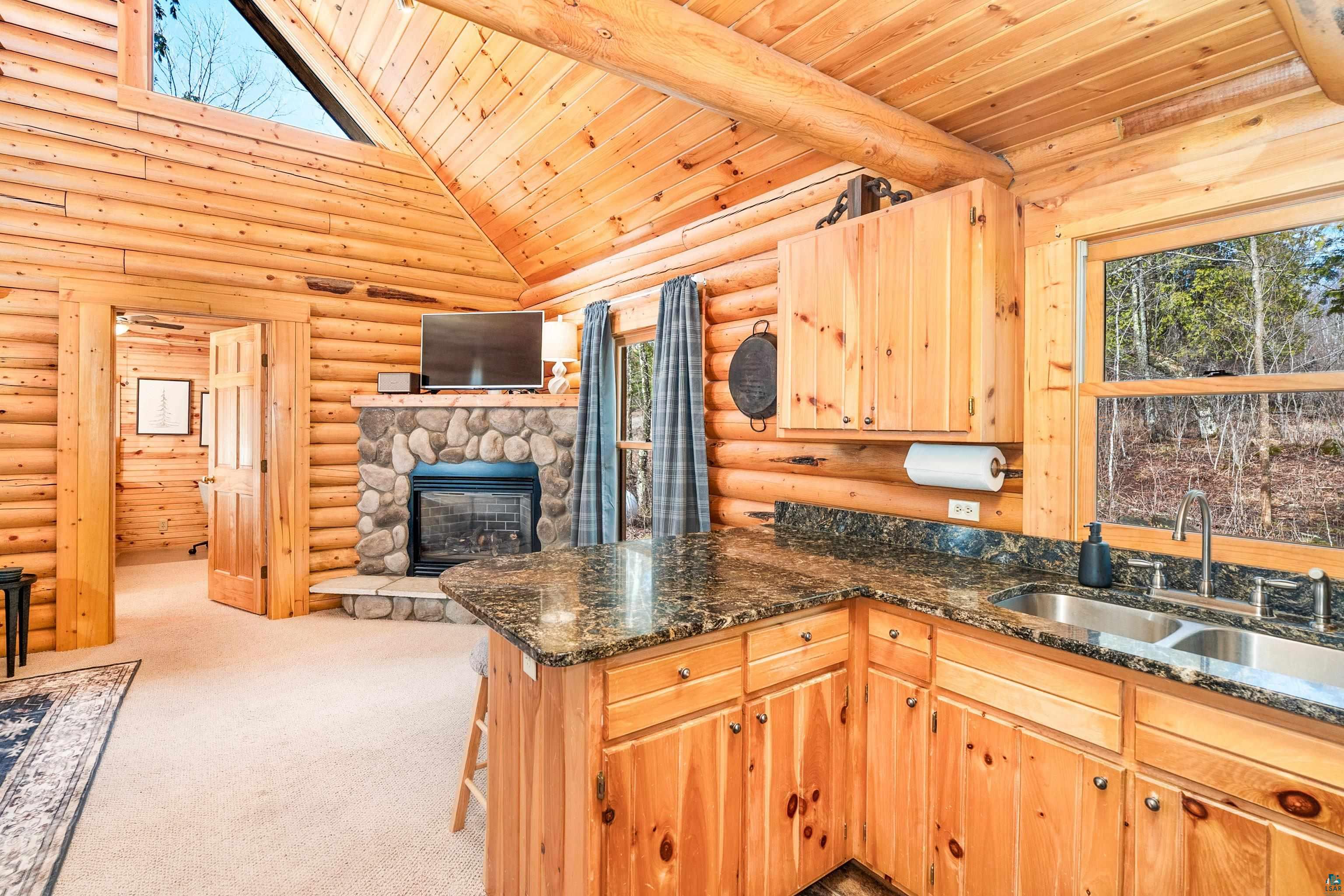 2659 Ridgeview Drive Two Harbors, MN 55616 - Photo 20 of 56 Log construction interior featuring a vaulted wood ceiling, a stone-clad fireplace, built-in wood cabinetry, a double basin stainless steel sink, and stone-finish countertops