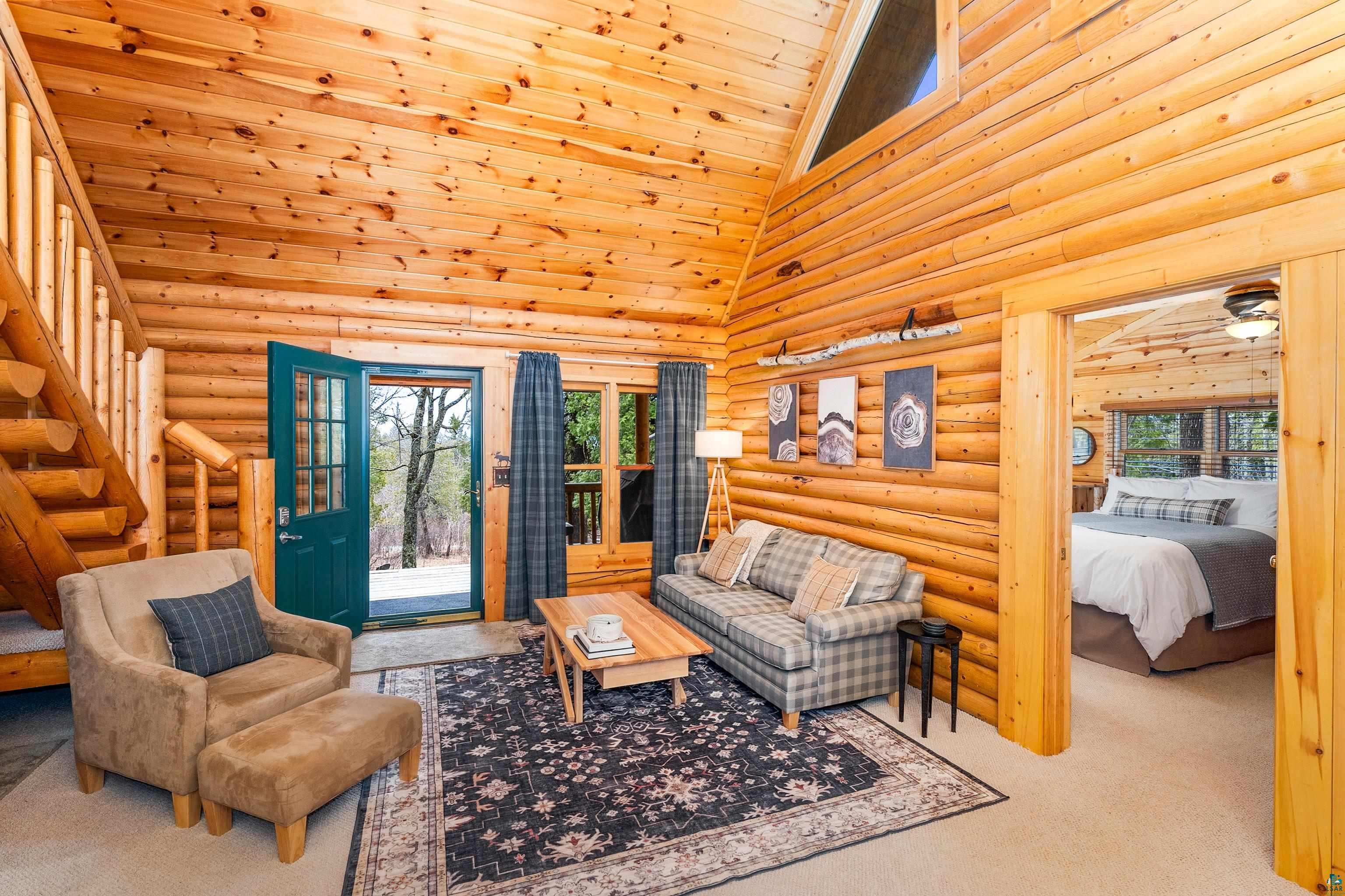 2659 Ridgeview Drive Two Harbors, MN 55616 - Photo 22 of 56 Open-concept living area featuring natural wood walls and ceiling, a prominent wood staircase, an exterior door with glass panels, a large window with exterior visibility, and an adjacent room accessible through a wide doorway