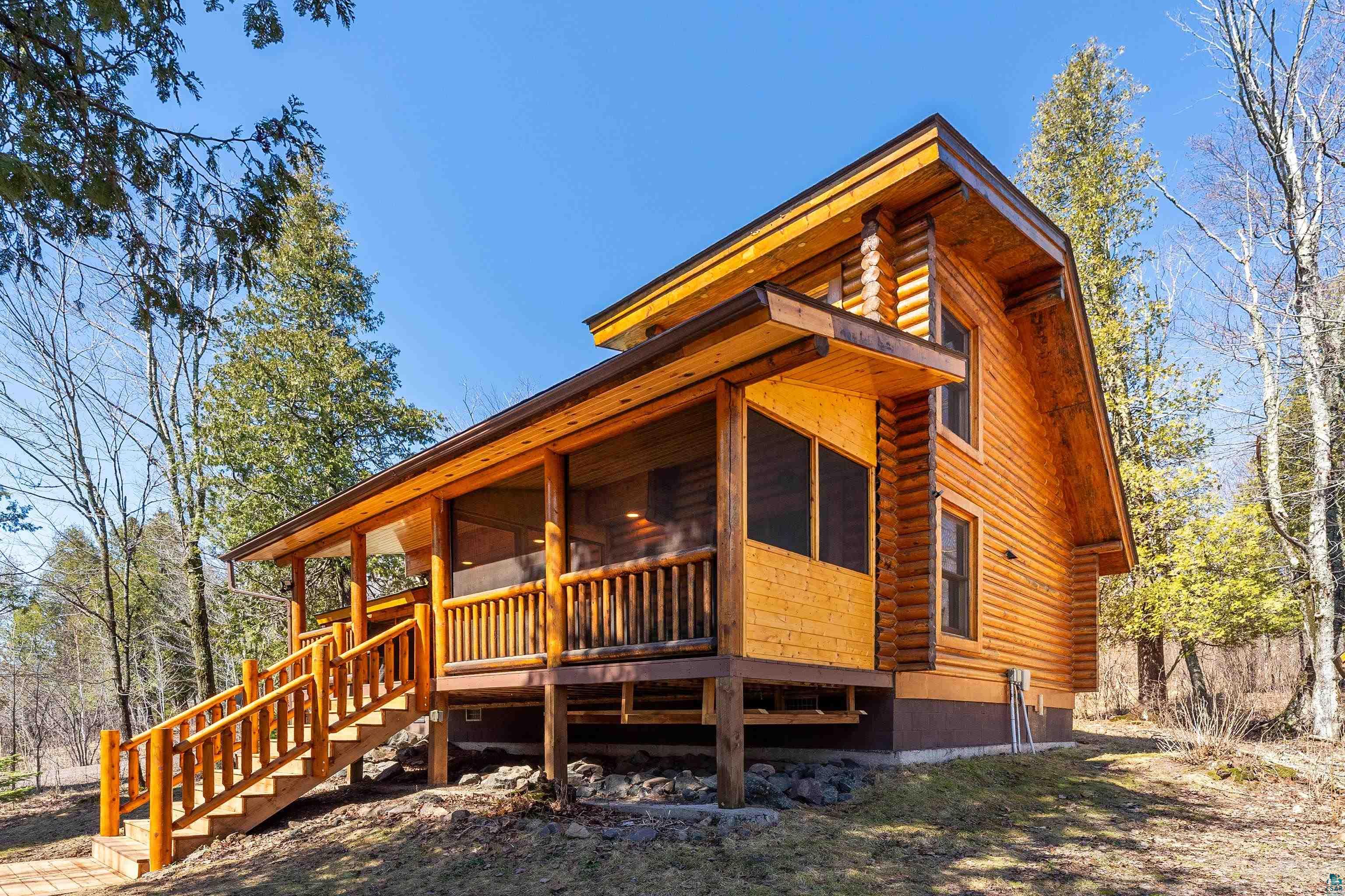2659 Ridgeview Drive Two Harbors, MN 55616 - Photo 4 of 56 Wood-clad cabin exterior featuring an elevated screened-in porch with wood railings and steps, multiple windows, and natural landscaping