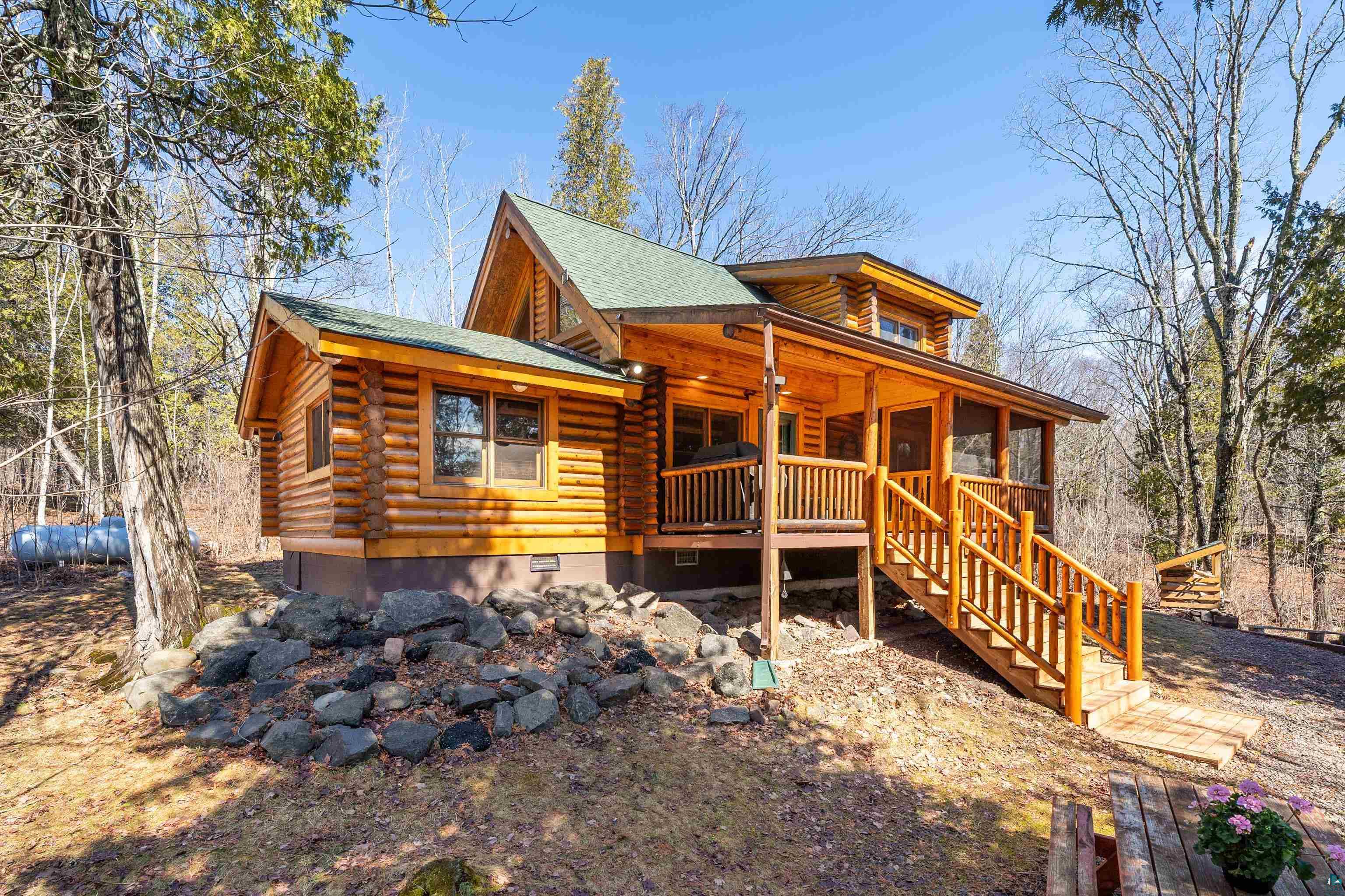 2659 Ridgeview Drive Two Harbors, MN 55616 - Photo 47 of 56 Log cabin exterior featuring a vibrant green shingle roof, natural wood siding, an elevated screened porch, a multi-level wooden staircase with railings, and a foundational rock landscaping detail