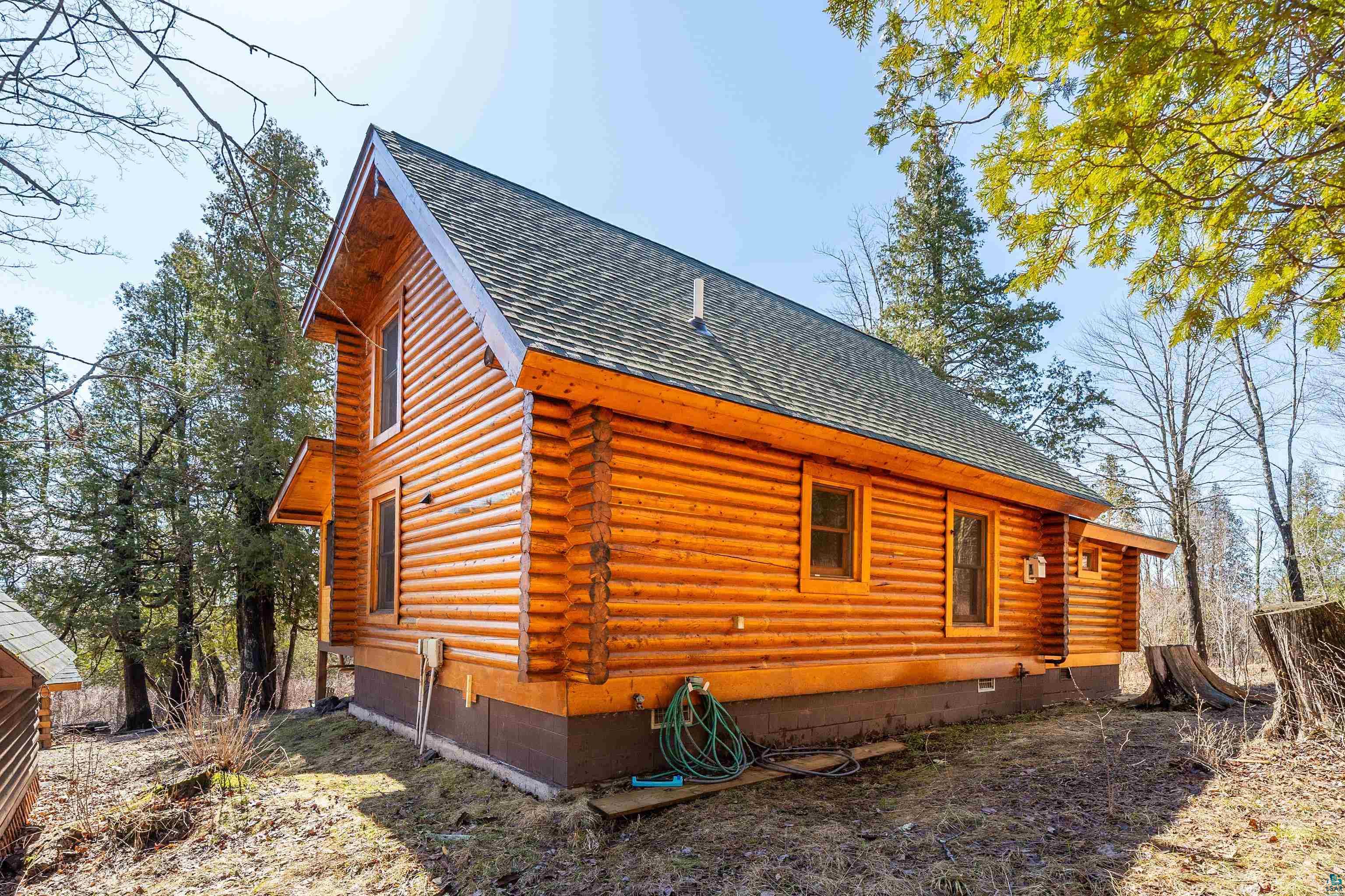 2659 Ridgeview Drive Two Harbors, MN 55616 - Photo 6 of 56 Log cabin exterior featuring a dark grey shingle roof, natural wood siding, multiple windows, and a dark brown foundation