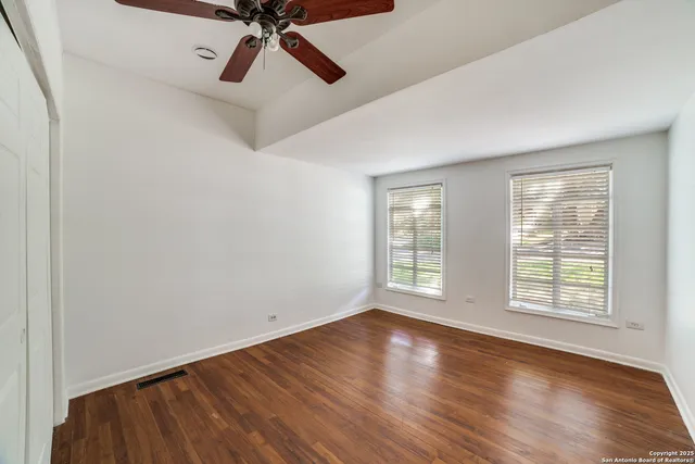 an empty room with wooden floor fan and windows