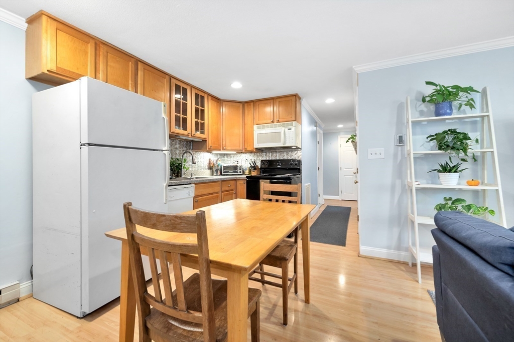 588 Main Street, Unit 3C Stoneham, MA 02180 - Photo 11 of 24 a kitchen with stainless steel appliances granite countertop a refrigerator a stove a dining table and chairs with wooden floor
