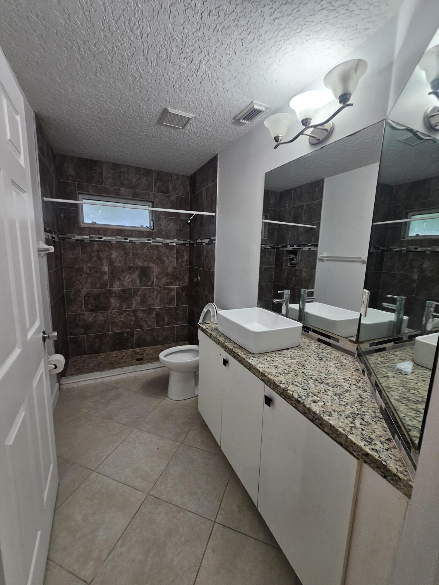 3215 Southeast Pinto Street Port St. Lucie, FL 34984 - Photo 18 of 34 a bathroom with a granite countertop sink a toilet a mirror and shower