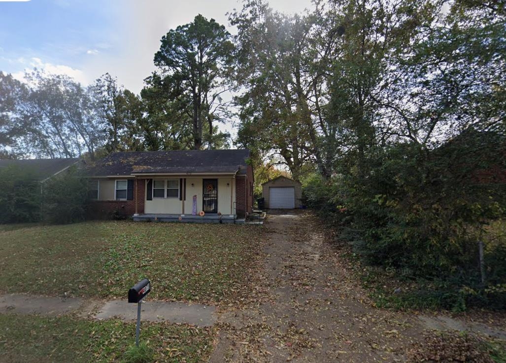 Single-story residence featuring brick and siding facade, a covered front porch with columns, a gravel driveway, and a detached garage structure