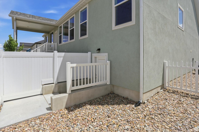 3636 West 910 South Syracuse, UT 84075 - Photo 60 of 70 Rear exterior of the property featuring a covered patio, light green stucco siding, white vinyl fencing, and a gravel-covered ground