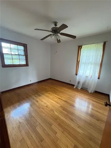 an empty room with wooden floor fan and windows