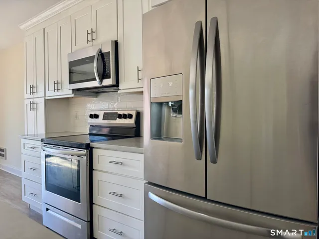 a kitchen with kitchen island a refrigerator stove a sink and white cabinets with wooden floor