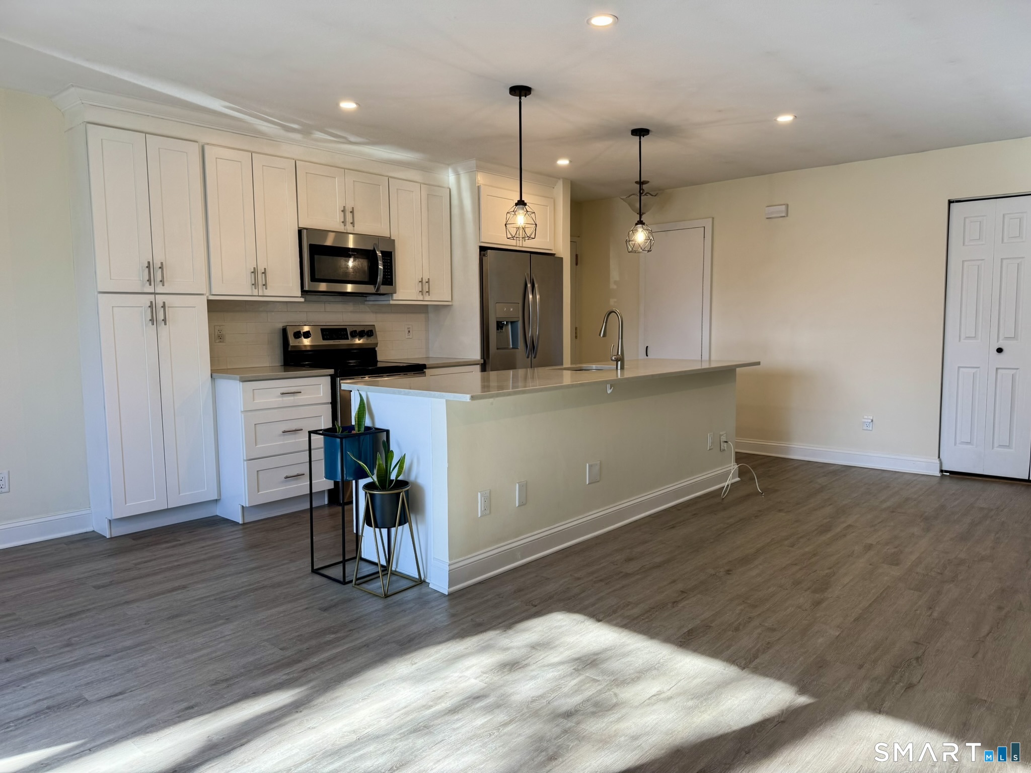 76 Maple Tree Avenue, Unit 6 Stamford, CT 06906 - Photo 7 of 27 a kitchen with kitchen island a refrigerator stove a sink and white cabinets with wooden floor