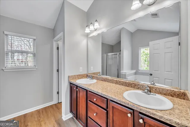 a bathroom with a granite countertop double vanity sink a mirror and a shower