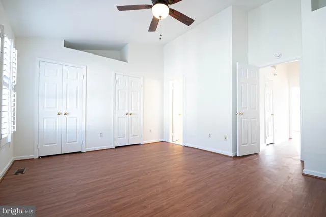 an empty room with wooden floor ceiling fan and windows