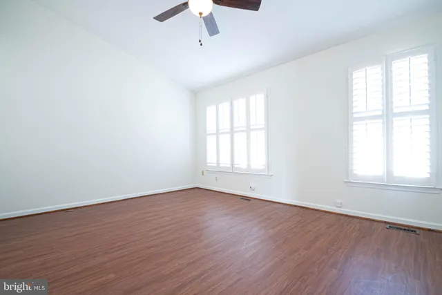 an empty room with wooden floor fan and windows