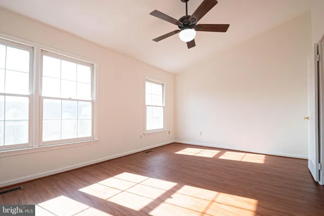 an empty room with wooden floor fan and windows