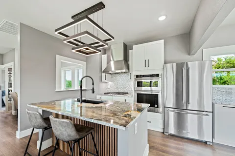 a kitchen with stainless steel appliances granite countertop a dining table chairs refrigerator and cabinets