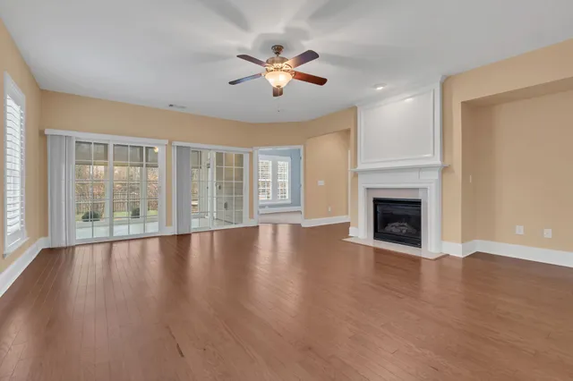an empty room with wooden floor fireplace and windows