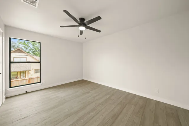 an empty room with wooden floor fan and windows