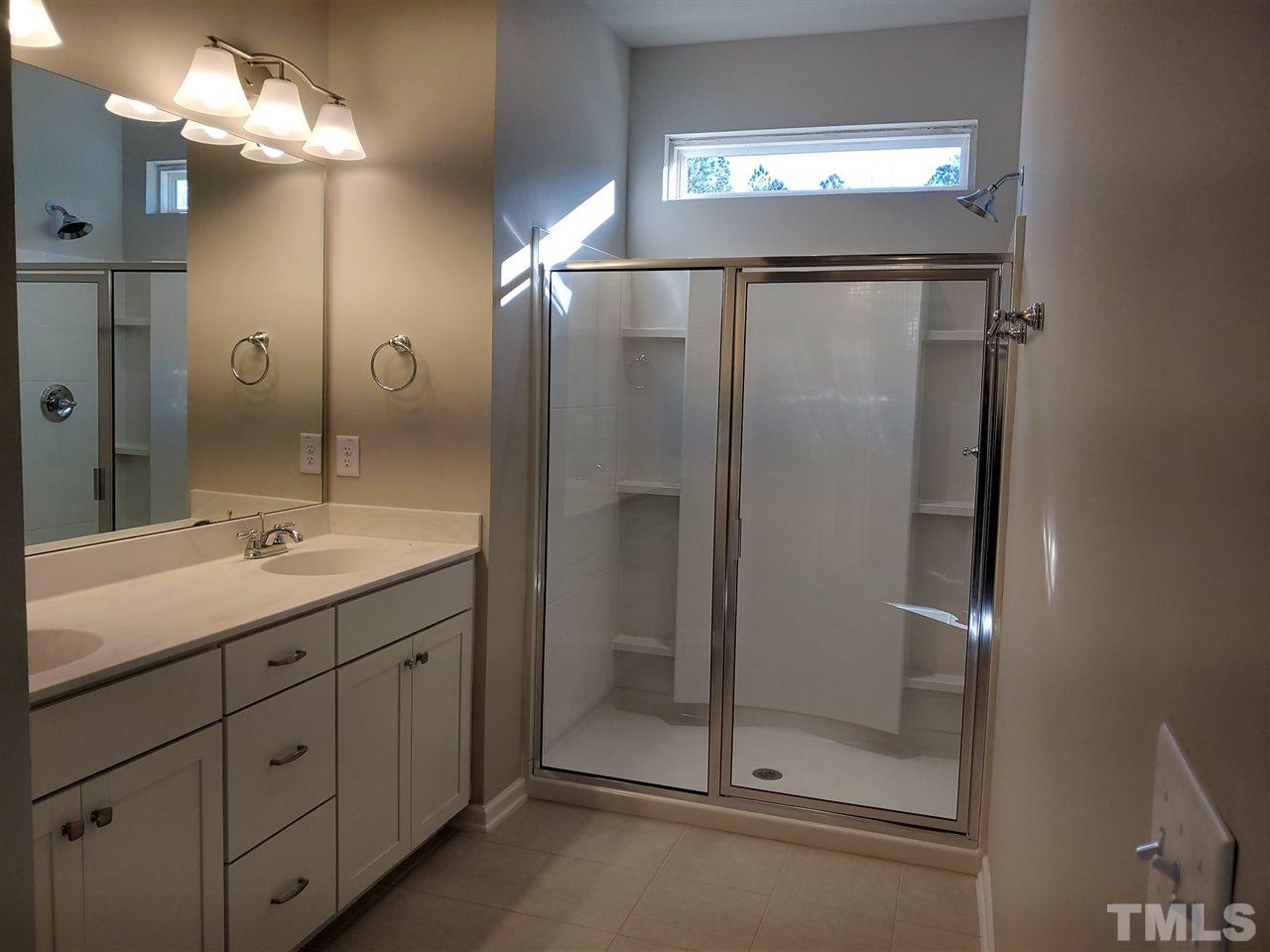 6339 Grace Lily Drive, Unit 18 Raleigh, NC 27607 - Photo 11 of 23 a bathroom with a mirror a sink and a glass door shower