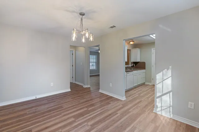 a view of an empty room with wooden floor and a kitchen