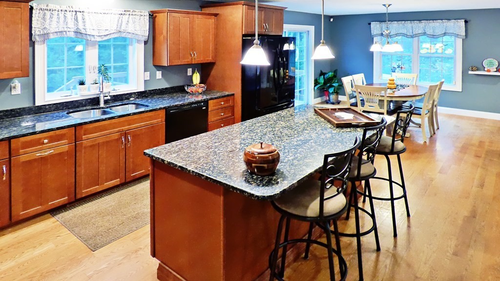255 Holmes Street Hanson, MA 02341 - Photo 8 of 34 a kitchen with stainless steel appliances kitchen island granite countertop a table chairs in it and wooden floors