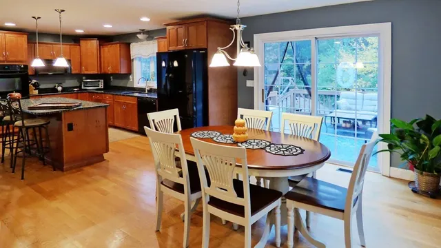 a kitchen with stainless steel appliances kitchen island granite countertop a refrigerator a sink a stove and a dining table with wooden floor