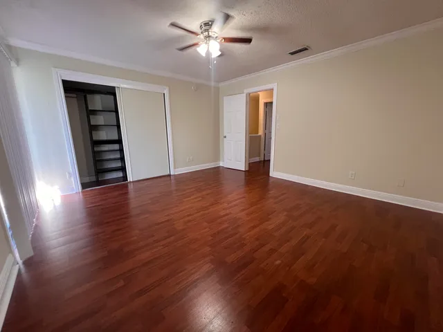 a view of an empty room with wooden floor and a ceiling fan