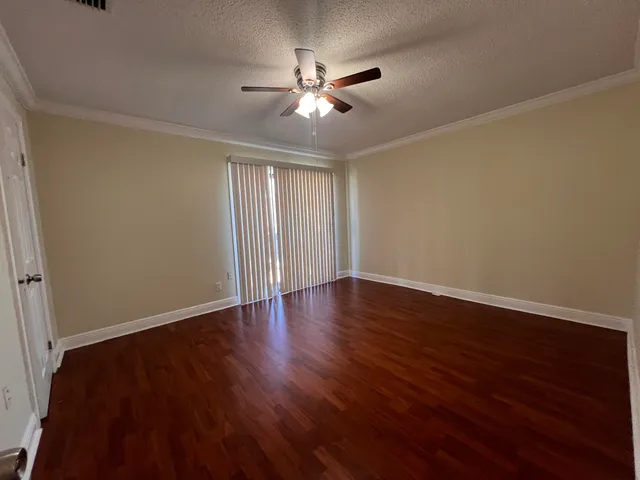 a view of an empty room with wooden floor and a ceiling fan