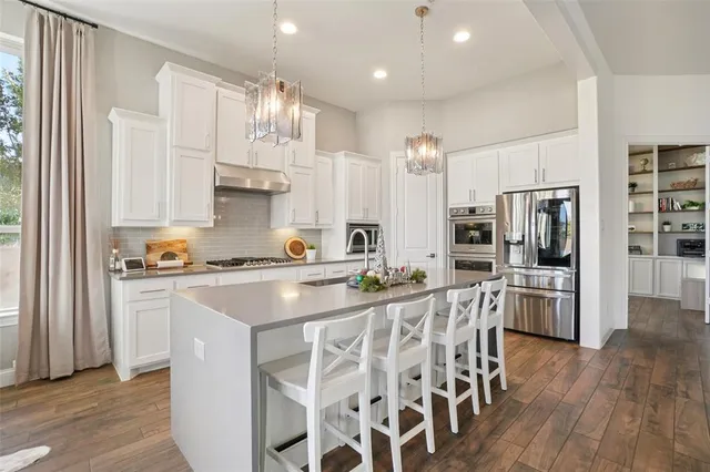 a kitchen with stainless steel appliances kitchen island granite countertop a refrigerator a stove a sink and white cabinets with wooden floor