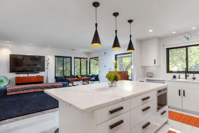 a large kitchen with stainless steel appliances a stove a sink dishwasher and a flat tv screen next to a window