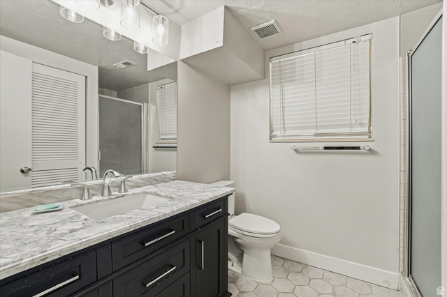 1025 Bristol Road Fruit Heights, UT 84037 - Photo 13 of 20 Bathroom featuring a dark wood vanity with a white countertop and undermount sink, hexagonal tile flooring, and a shower with a clear glass enclosure